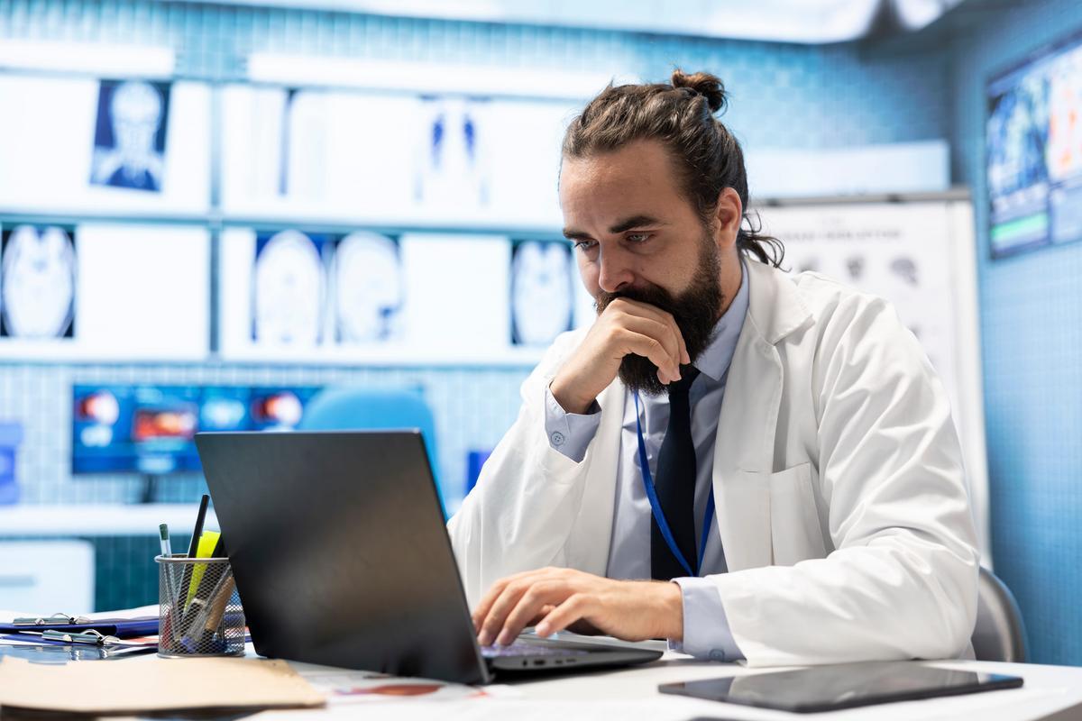 Clinician reviewing records on a laptop while wearing a badge lanyard.