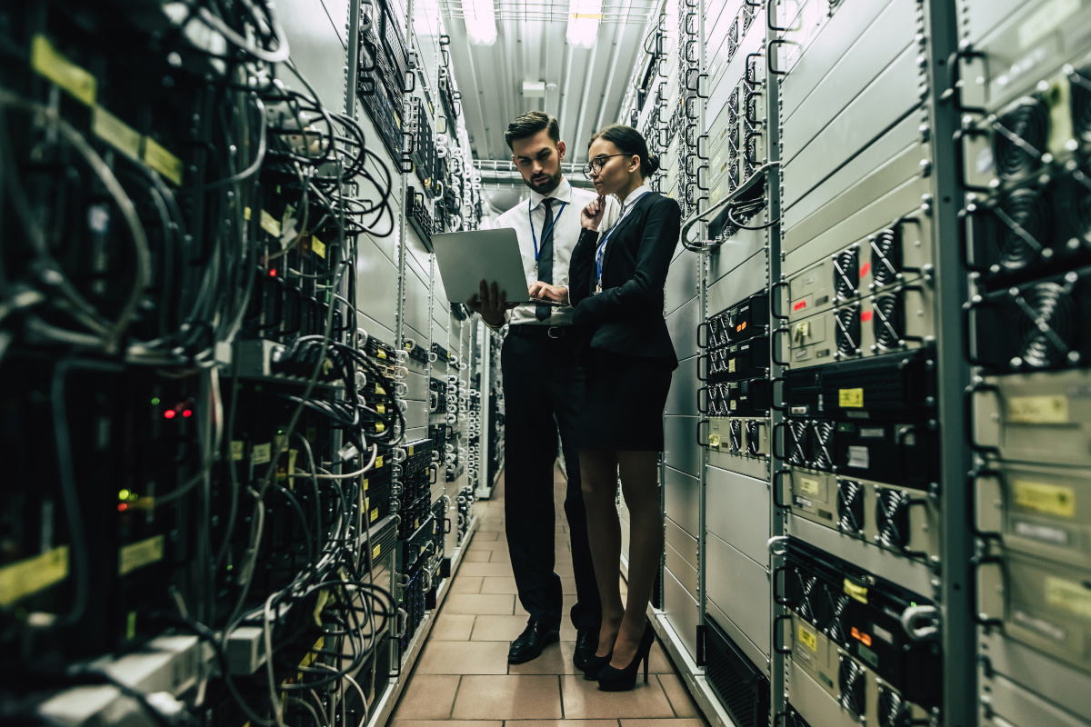 Two employees standing in front of hardware with a laptop providing assessments and management